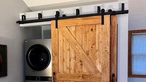 A room with a wooden sliding door, two stacked washing machines, and a white chair.