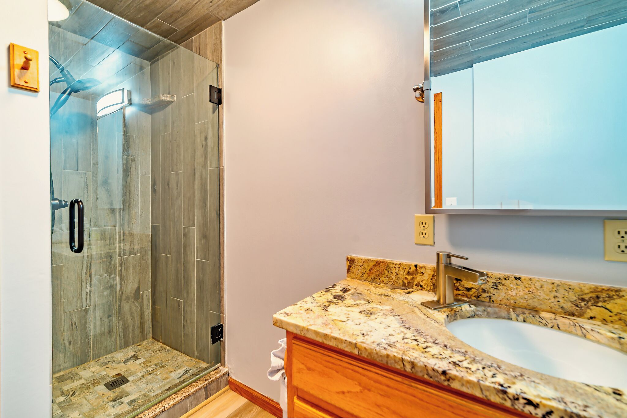 Un baño moderno con cabina de ducha de vidrio, encimera de granito y un espejo grande.