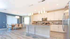 Een moderne keuken met witte kasten, roestvrijstalen apparatuur en een centraal eiland met barstoelen.