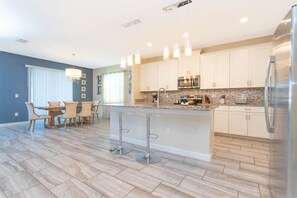 A modern kitchen with white cabinets, stainless steel appliances, and a central island with bar stools. - Lakefront Pool & Spa | Steps to Clubhouse | Prime Storey Lake Location (Kissimmee)