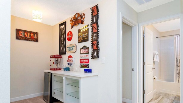 A hallway with a white wall, a cinema-themed decoration, a popcorn machine, and a door leading to a bathroom.