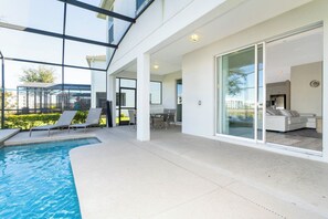 A modern outdoor pool area with lounge chairs, a dining table, and a glass-enclosed living space. - Lakefront Pool & Spa | Steps to Clubhouse | Prime Storey Lake Location (Kissimmee)