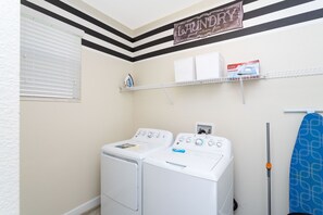 A laundry room with a washing machine, a dryer, and a shelf with laundry supplies. - Lakefront Pool & Spa | Steps to Clubhouse | Prime Storey Lake Location (Kissimmee)