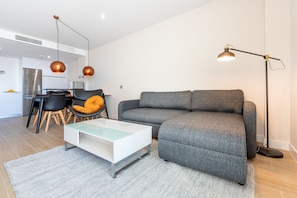 Una sala de estar moderna con un sofá gris, una mesa de centro blanca y una zona de comedor con una silla negra y una mesa.