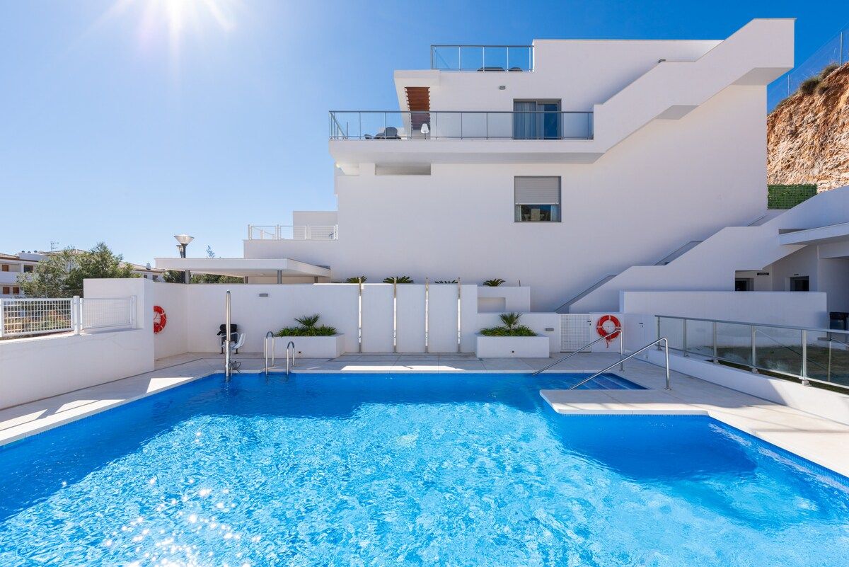 A modern building with a swimming pool, multiple balconies, and a clear sky.