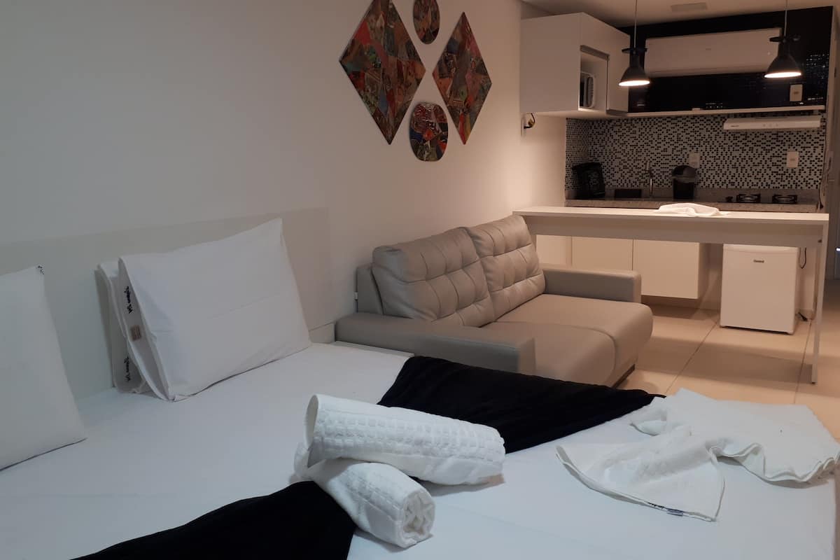 A modern hotel room with a bed, a sofa, a small kitchenette, and a dining area.