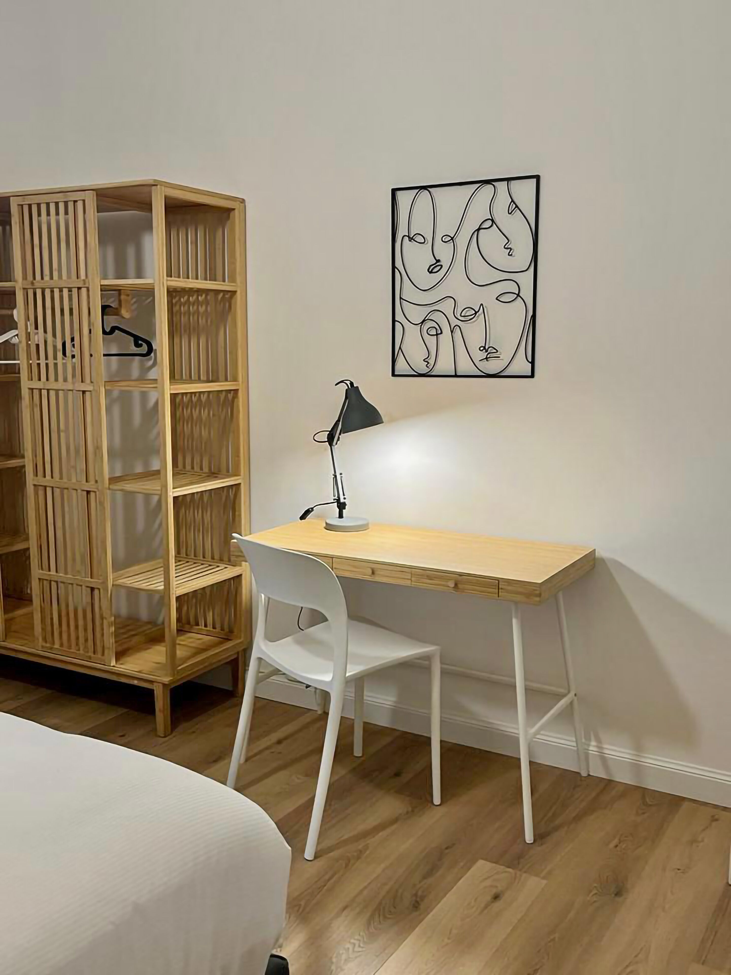 A room with a wooden desk, white chair, and a hanging artwork.