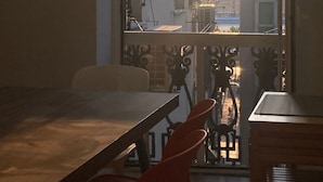 A dining area with a table and chairs, a window with a view of buildings and a sunset. - Happy Family Apartments Lanterna (Genoa)