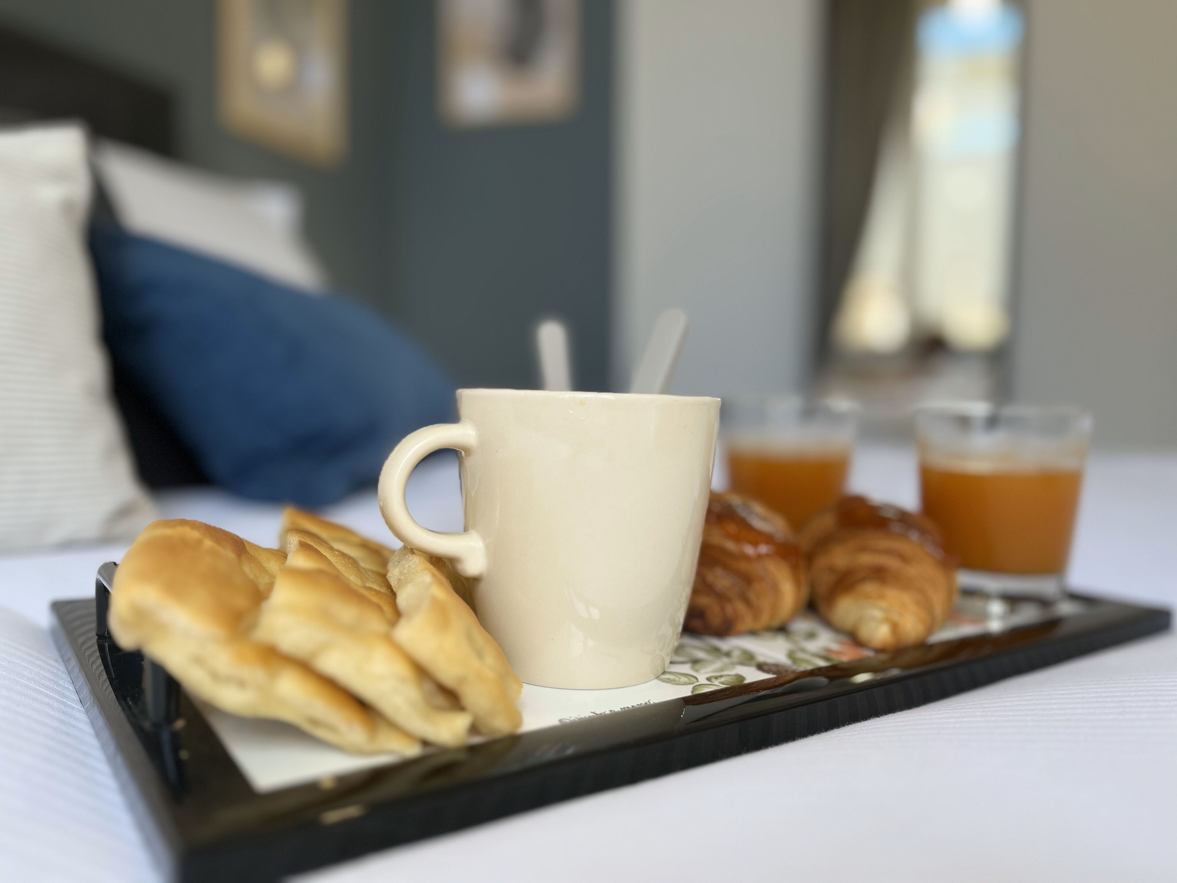 A tray with pastries, a mug, and two glasses of orange juice on a bed.