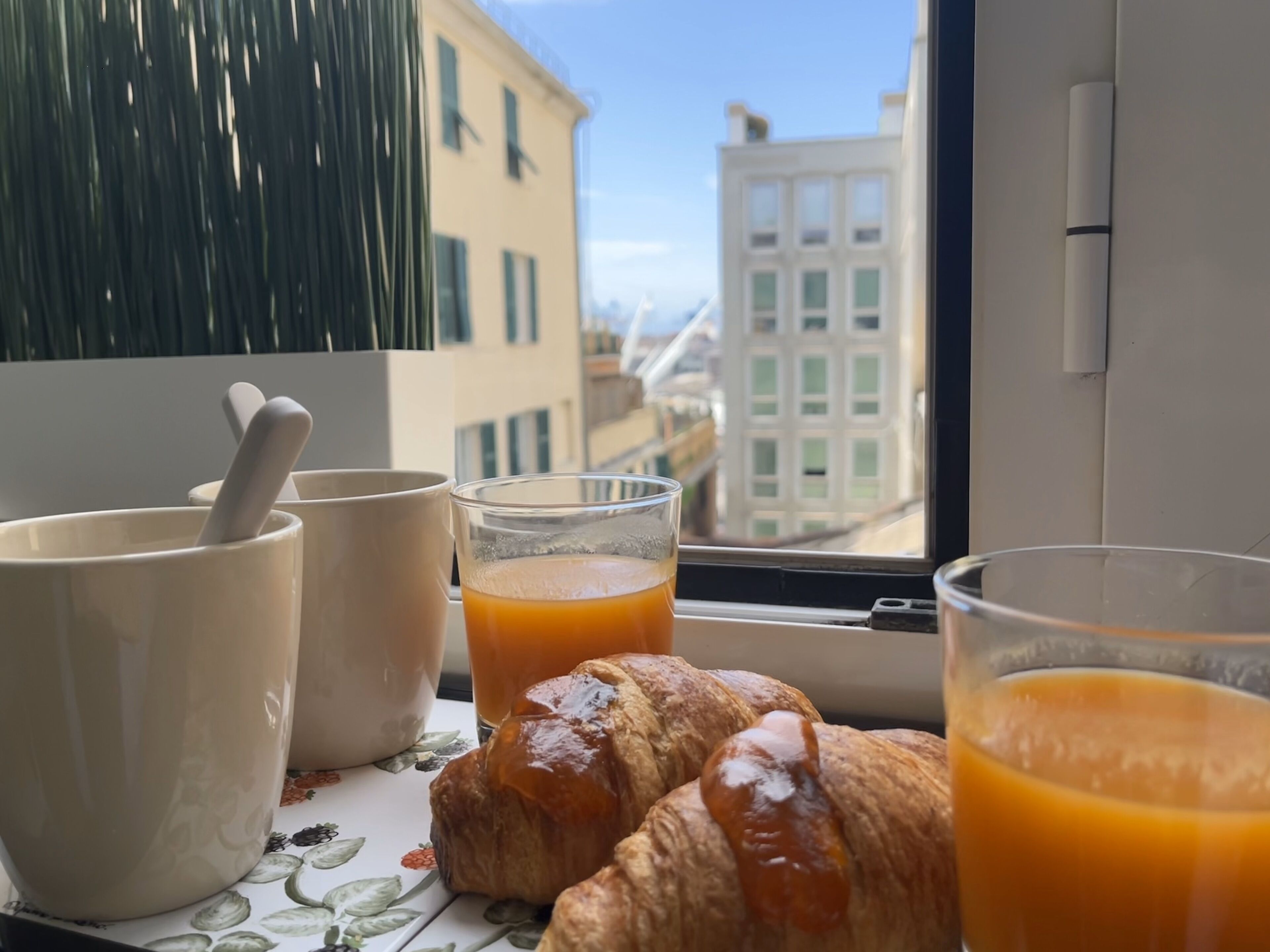 A breakfast setup with croissants and orange juice on a table by a window overlooking a cityscape.