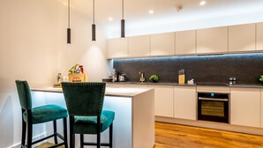 Una cucina moderna con isola centrale, due sgabelli da bar, illuminazione a sospensione e forno integrato.