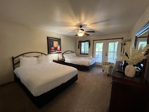 A bedroom with two beds, a ceiling fan, a framed picture, a window, and a door leading to an outdoor area. - Lake view three bedroom, three bath Harbor North luxury cottage with private hot tub overlooking Lake Ouachita. by RedAwning (Mount Ida)