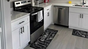 A modern kitchen with white cabinets, stainless steel appliances, and a black and white kitchen mat. - Home in Kissimmee (Kissimmee)