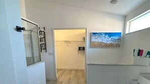 A modern bathroom with a shower, a toilet, and a sink. There is a painting on the wall and a small shelf with toiletries. - Home in Kissimmee (Kissimmee)