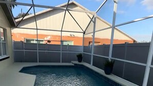 An indoor swimming pool with a clear view of the surrounding area, including a building with a sloped roof and a fenced perimeter. - Home in Kissimmee (Kissimmee)