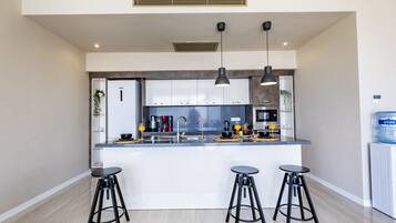A modern kitchen with a central island, bar stools, pendant lighting, and a water dispenser.