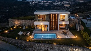 A modern two-story house with a swimming pool, stone walls, and outdoor seating.