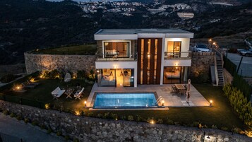 Uma casa moderna de dois andares com piscina, paredes de pedra e área de estar ao ar livre.