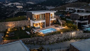 A modern two-story house with a swimming pool, stone walls, and outdoor furniture.