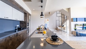 A modern kitchen with dark cabinets, a central island, and a dining area with a TV and seating.