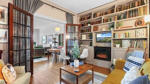 A cozy living room with a fireplace, a bookshelf, and a dining area. - Downtown Apartment! Large, Cozy, Family friendly private oasis in city center! (Petoskey)