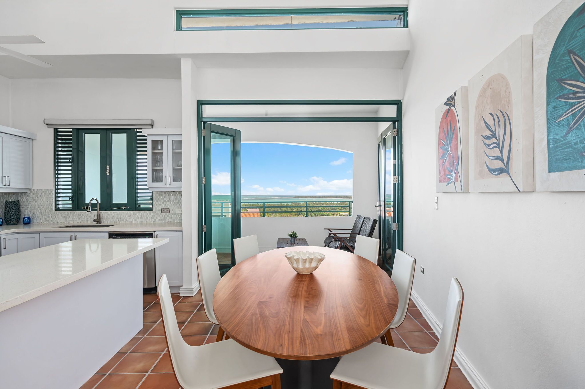 A modern kitchen with a large island, white cabinetry, and a view of the outdoors.