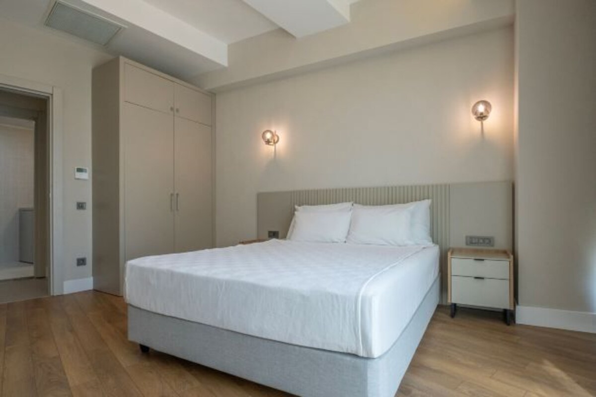 A bedroom with a large bed, two bedside tables, a wardrobe, and two wall-mounted lights.