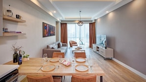 A modern living room with a dining area, a sofa, a TV, and a bookshelf. - Sirius Town Residence and Spa (Antalya)