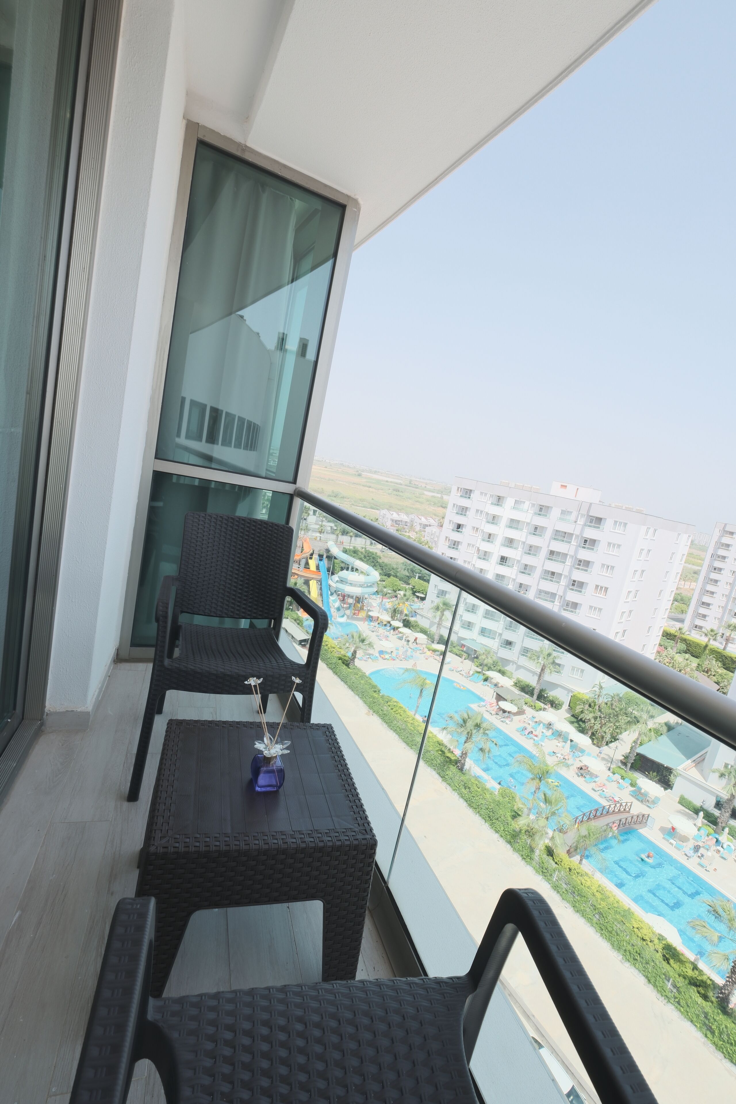 A balcony with a table and chairs, overlooking a swimming pool and buildings.