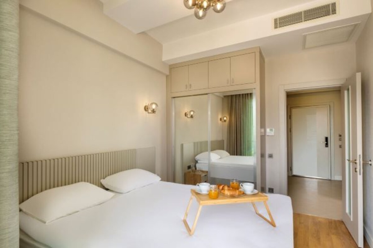 A hotel room with a bed, a bedside table with a tray of breakfast items, a wardrobe, and a mirror.