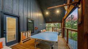 A ping pong table in a wooden deck area with a view of trees and a sunset. - Cozy, Game Deck, Outdoor Swing, 2 King Suites, Save 7% in Taxes! (Broken Bow)
