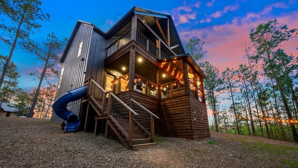 A wooden cabin with a balcony, a slide, and string lights. - Cozy, Game Deck, Outdoor Swing, 2 King Suites, Save 7% in Taxes! (Broken Bow)