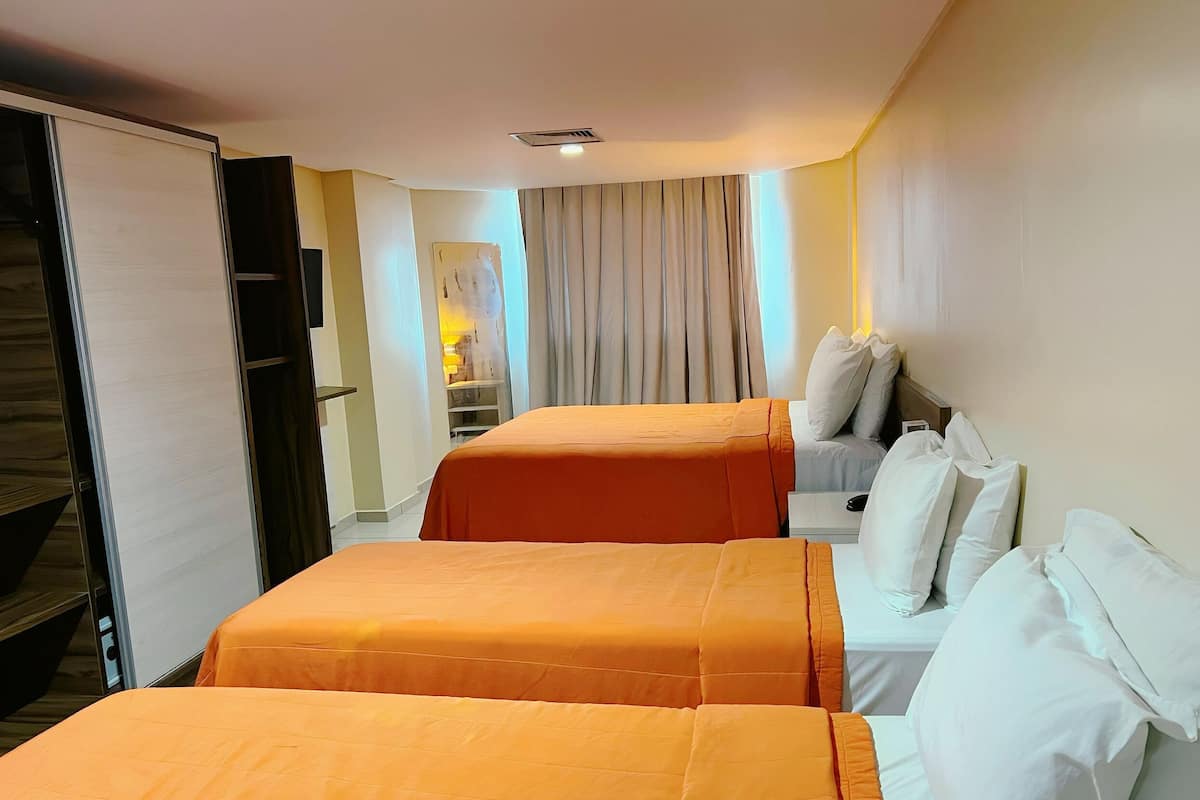 Habitación de hotel con dos camas, un escritorio, una silla y un ventanal con cortinas.