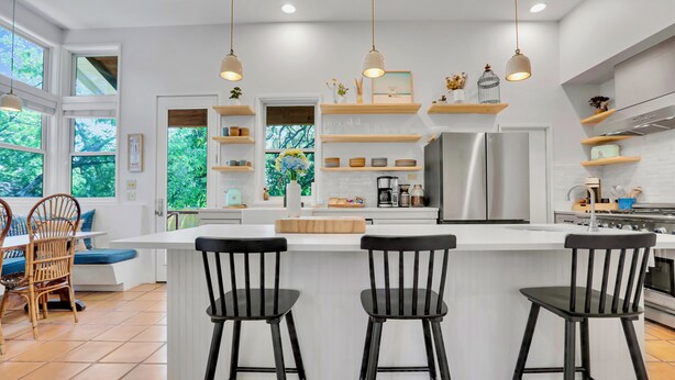 Une cuisine moderne dotée d’un îlot central, de tabourets de bar noirs et de luminaires suspendus.