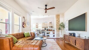 Un salon moderne avec un canapé en cuir, une table basse, une bibliothèque et un grand téléviseur à écran plat.