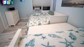 Une chambre avec deux lits, une télévision, une commode et une fenêtre avec des stores.