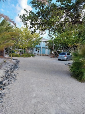 A two-story house with a gravel driveway and a parked car. - Sonscape's Cozy 1-Bdr 1-Bath Private Guest Suite Opens Right Onto the Beach! (Cayman Brac)