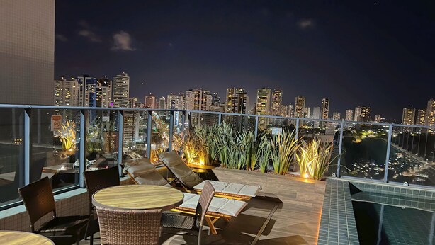 A rooftop terrace with outdoor seating, a city skyline view, and a glass railing. - Miramar One Way Tambaú (João Pessoa)
