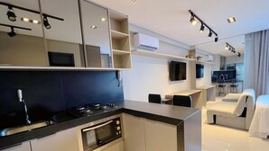 A modern hotel room with a kitchenette, a flat-screen TV, a sofa, and a bed. - Miramar One Way Tambaú (João Pessoa)
