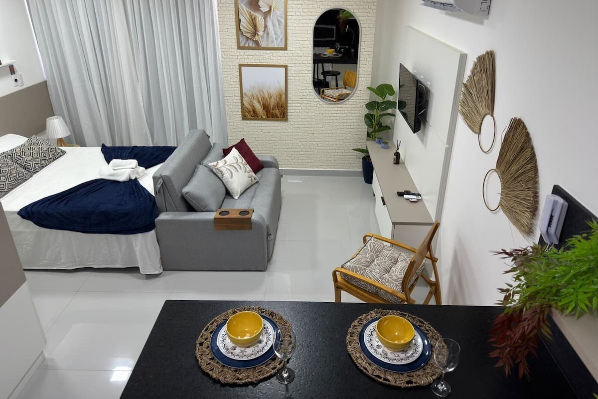 Een moderne woonkamer met een grijze bank, een eettafel met twee gele kommen, een televisie en een spiegel.