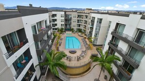 Un moderno edificio de apartamentos con piscina central rodeada de zonas de descanso y palmeras.