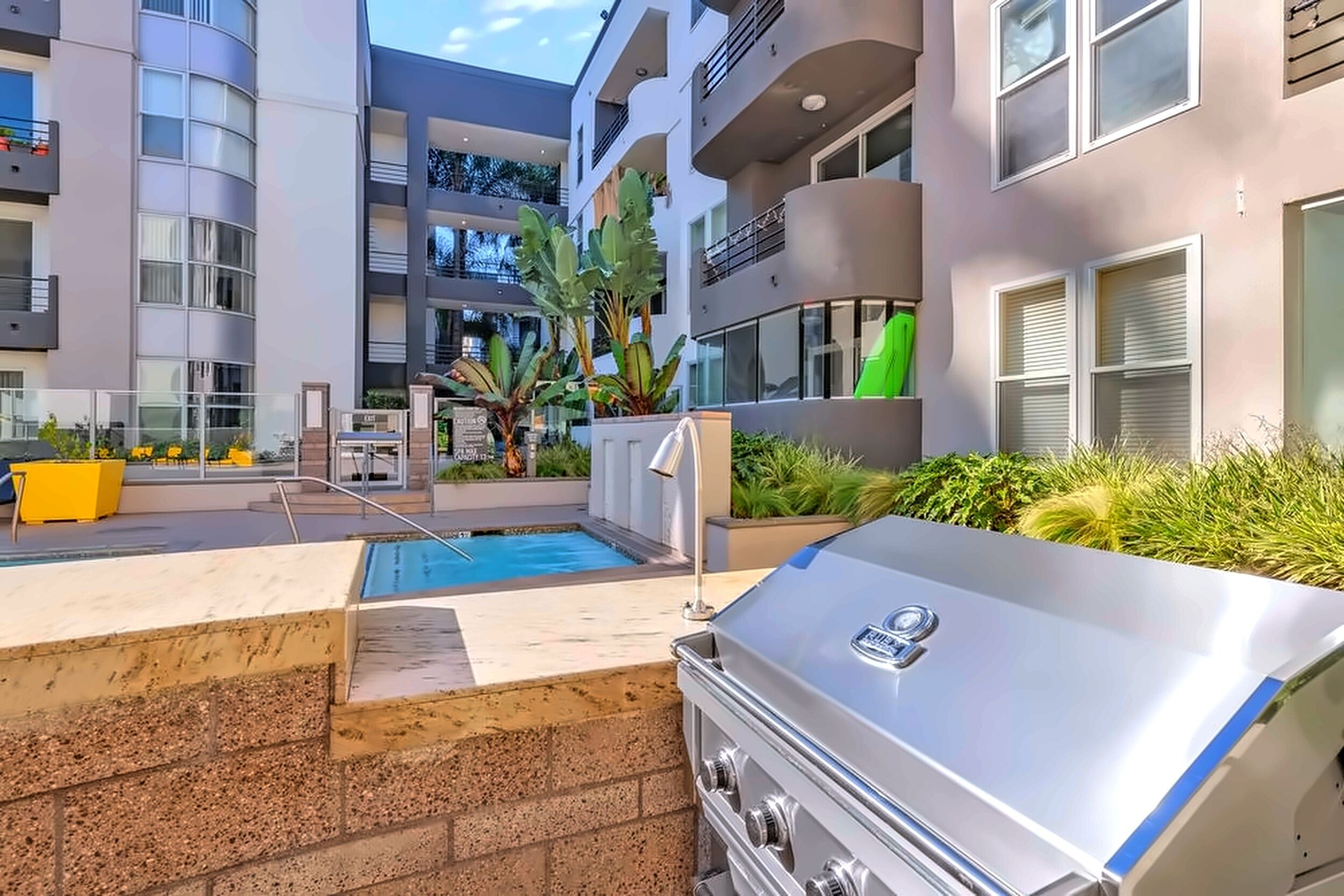 Zona de piscina moderna al aire libre con una parrilla, rodeada de edificios de apartamentos.