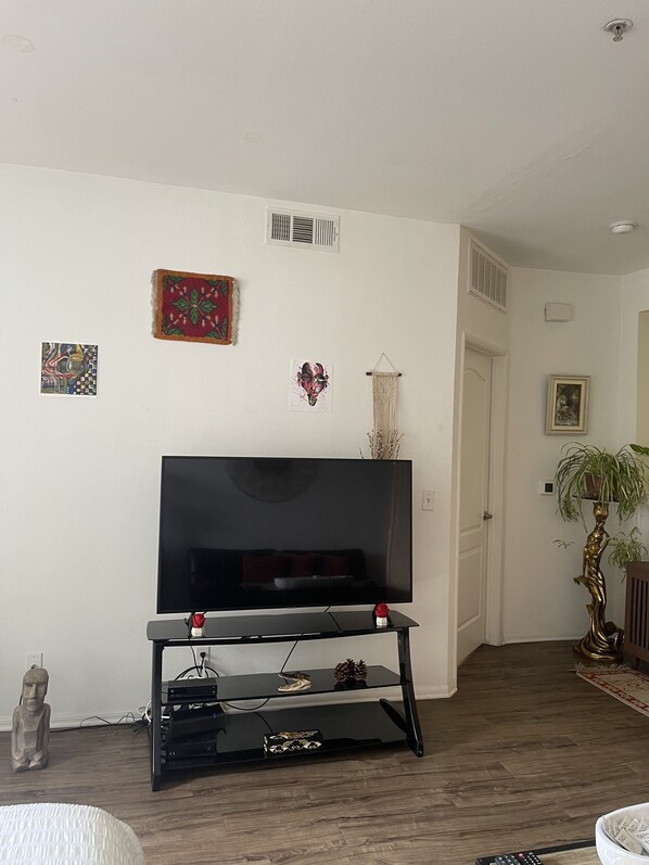 A living room with a flat-screen TV on a black stand, a statue, and wall art.