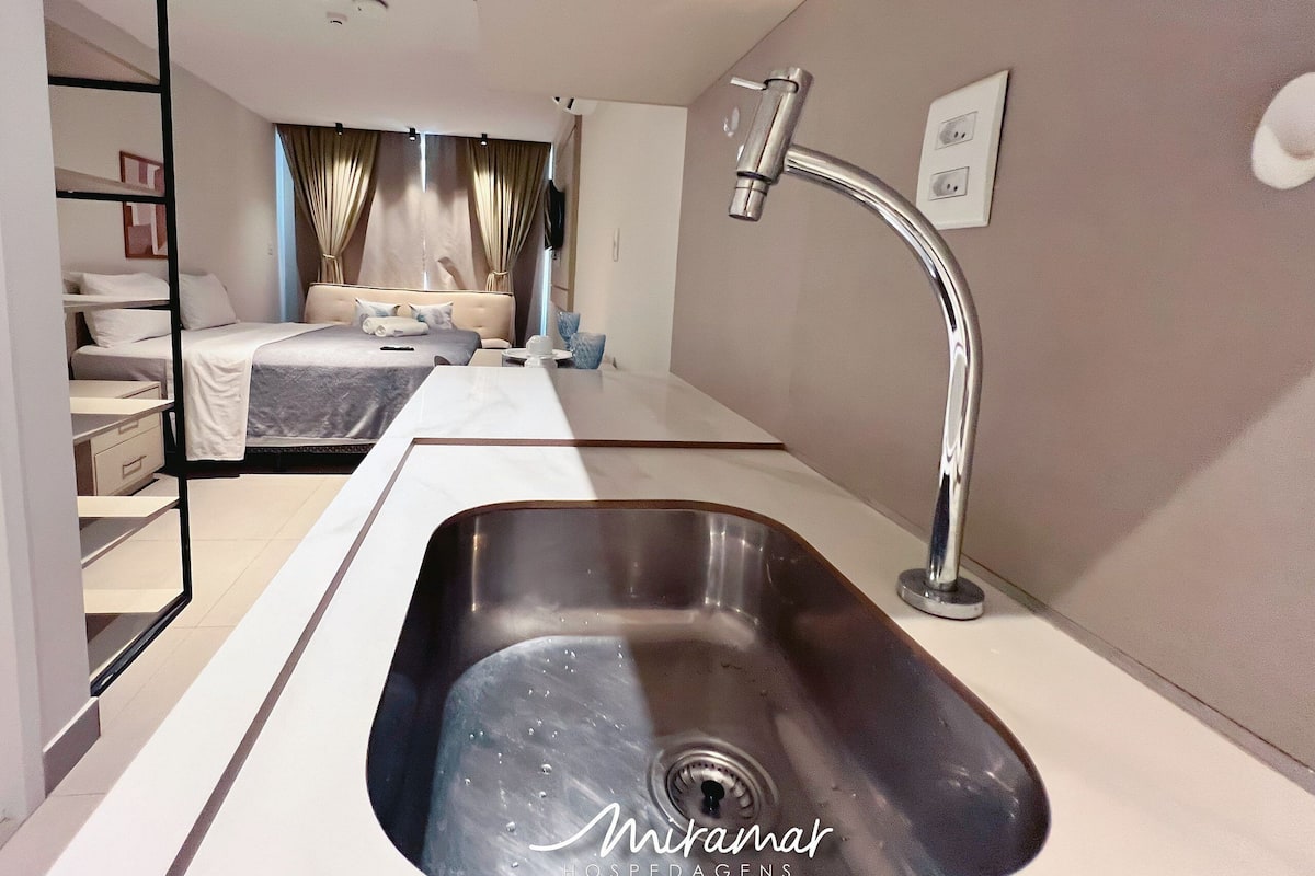 A modern hotel room with a large bed, a built-in wardrobe, a bathroom with a sink and shower, and a view of the city.