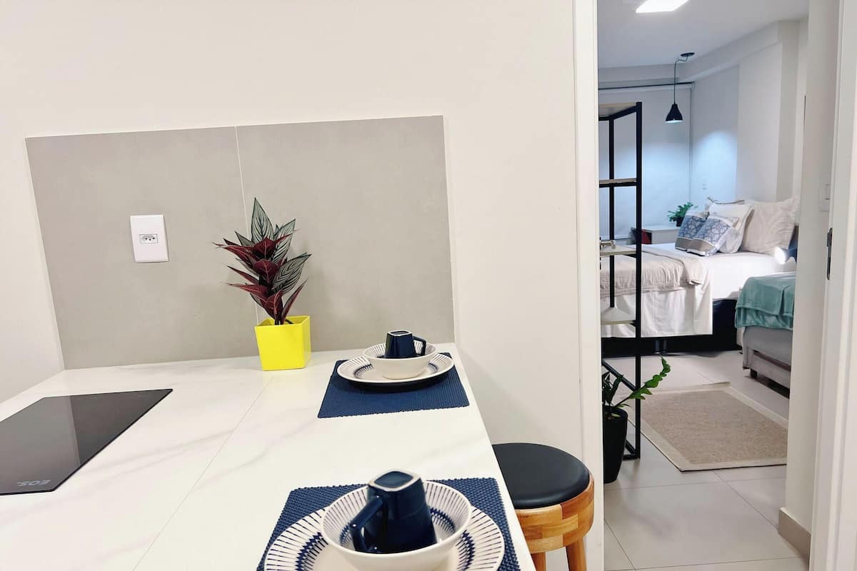 A compact room with a bed, a desk with a laptop, a small table with a plant, and a chair.