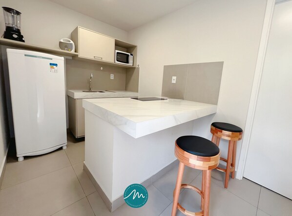 Una cocina compacta con refrigerador, microondas y una pequeña isla con taburetes.