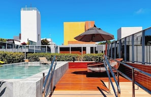 A rooftop pool with a wooden deck, lounge chairs, and a large umbrella. - Miramar Vida do Mar (João Pessoa)