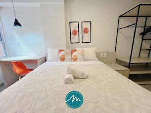 Una habitación de hotel con una cama, un escritorio, una silla naranja y una litera.