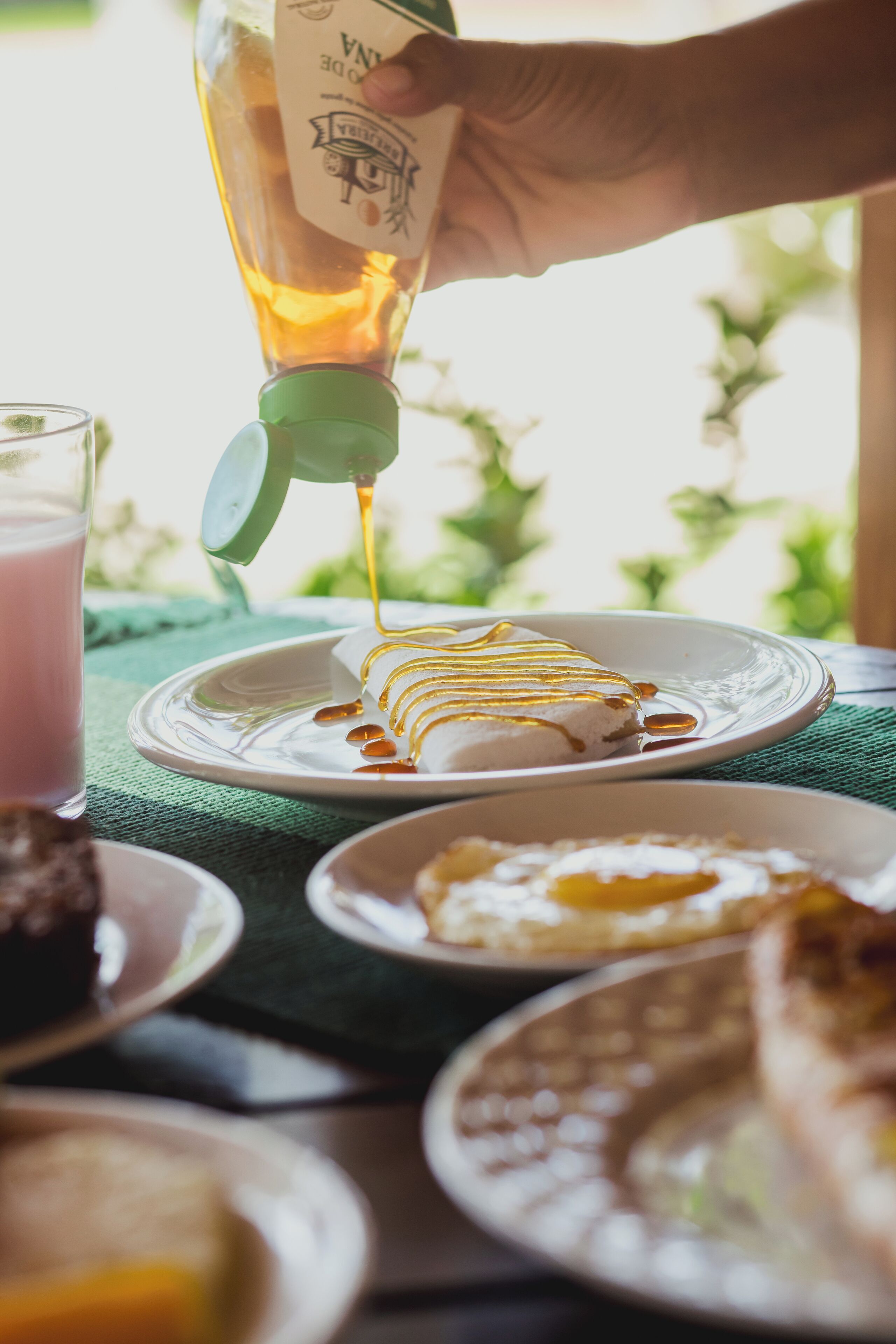 A hand pouring syrup onto a dessert on a plate.