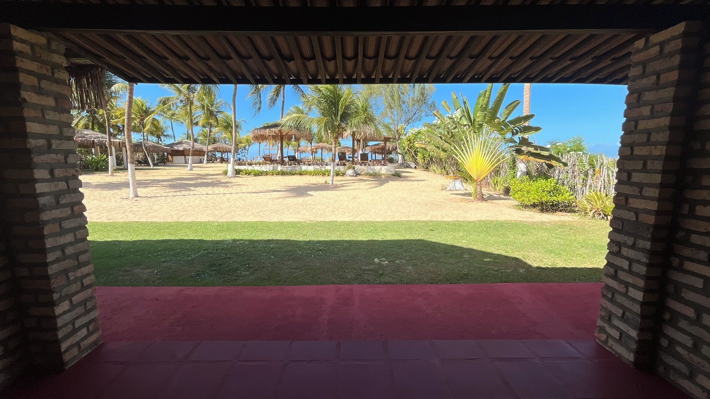 Une terrasse couverte offrant une vue sur une plage de sable et des palmiers.